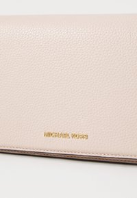 Šviesiai rožinė odinė piniginė su tekstūruota paviršiumi, su auksiniu "MICHAEL KORS" logotipu ir siūlėmis, suteikiančiomis švarų ir paprastą dizainą.