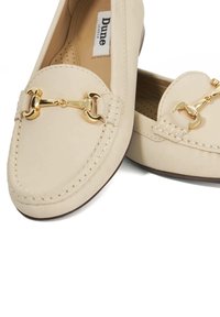 Beige leren loafers met een goudkleure accent van een paardenbit, moccasinstiksel, en een gestructureerde binnenzool, met een ronde neus en platte zool.