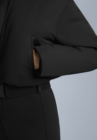 Czarna kurtka puchowa o strukturalnym kroju, z teksturowanej tkaniny i kieszenią boczną. Akcentowana dopasowanym, prążkowanym paskiem w talii.