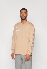 Bež sako dugih rukava s bijelim Nike logotipom i grafikom Chicago Bullsa na prsima. Sivi zvezdasti uzorak na lijevom rukavu. Materijal: pamuk.