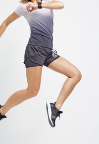 Conjunto deportivo que presenta una camiseta de manga corta en un degradado gris y pantalones cortos gris oscuro; tejido texturizado, diseño elegante; zapatillas deportivas negras.