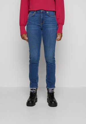 Mėlyni liekni džinsai, pagaminti iš džinsinio audinio, su aukštu liemeniu, penkiomis kišenėmis ir siuvinėjimo detalėmis, derinami su juodomis botais ir rožiniu ilgomis rankovėmis viršutiniu drabužiu.