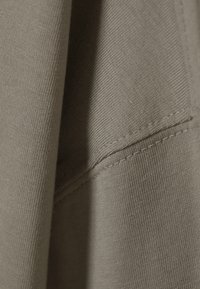 Licht olijfgroene stof met een gladde textuur, met een zichtbare naad en stikseldetails. Close-up van lichtgewicht, rekbaar materiaal.