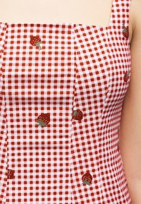 Κόκκινο και λευκό καρό φόρεμα με μικρά σχέδια φράουλας, με τετράγωνο ντεκολτέ και τιράντες σε ένα άτομο.