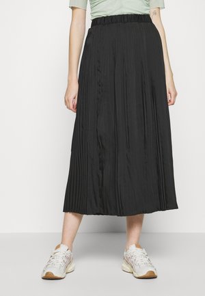 Jupe midi plissée noire avec une taille élastique, texture lisse et design fluide, associée à des baskets légères sur un fond neutre.