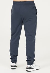 Marina blå mjukisbyxor i ett mjukt, elastiskt material, med sidofickor och resårmidja, i kombination med vita sportskor.