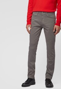 Pantalones de algodón grises con corte slim, que cuentan con cierre frontal de botón y cremallera, bolsillos laterales y detalles de costura sutiles.