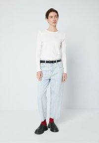 Vit långärmad tröja, ljusblå baggy jeans, svart bälte, röda strumpor och svarta slip-in skor. Enkel design, inga mönster eller logotyper.