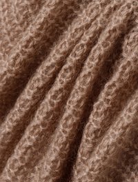 Strickstoff in sanften, hellbraunen Farbtönen mit einem strukturierten, gerippten Muster, das ein feines,flaumiges Aussehen und einen leichten Glanz zeigt.