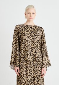 Halenka s leopardím potiskem a dlouhými rukávy, vyrobená z lehkého materiálu, s kulatým výstřihem a volným střihem. Zemité béžové a černé barvy.