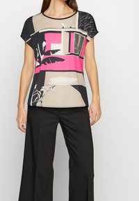 Blusa a maniche corte con un design geometrico in rosa, beige e nero, con accenti floreali e vestibilità ampia, realizzata in tessuto leggero.