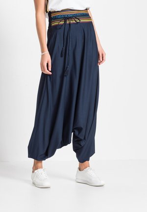 Pantaloni harem blu con una cintura elastica colorata e testurizzata; tessuto leggero; vestibilità ampia con un design a cavallo abbassato; abbinati a sneakers bianche.