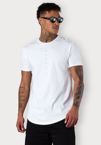 White cotton t-shirt featuring a vertical mint green print. Short sleeves and a crew neck, paired with black sunglasses. Slightly curved hem.