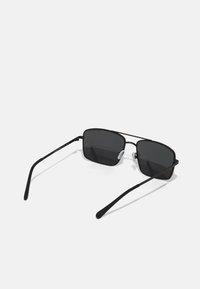 Ochelari de soare negri din metal, cu lentile rectangulare și brațe subțiri, elegante. Prezintă suporturi transparente pentru nas și un branding subtil pe templu.