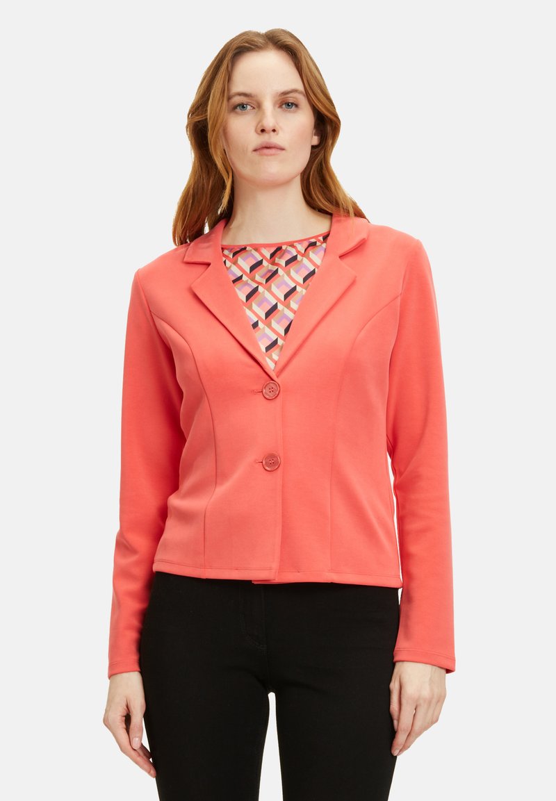 Koralfarbenes Blazer mit langen Ärmeln und Spitzkragen, ausgestattet mit zwei Knöpfen und einer strukturierten Passform. Das Innenshirt hat ein geometrisches Muster.