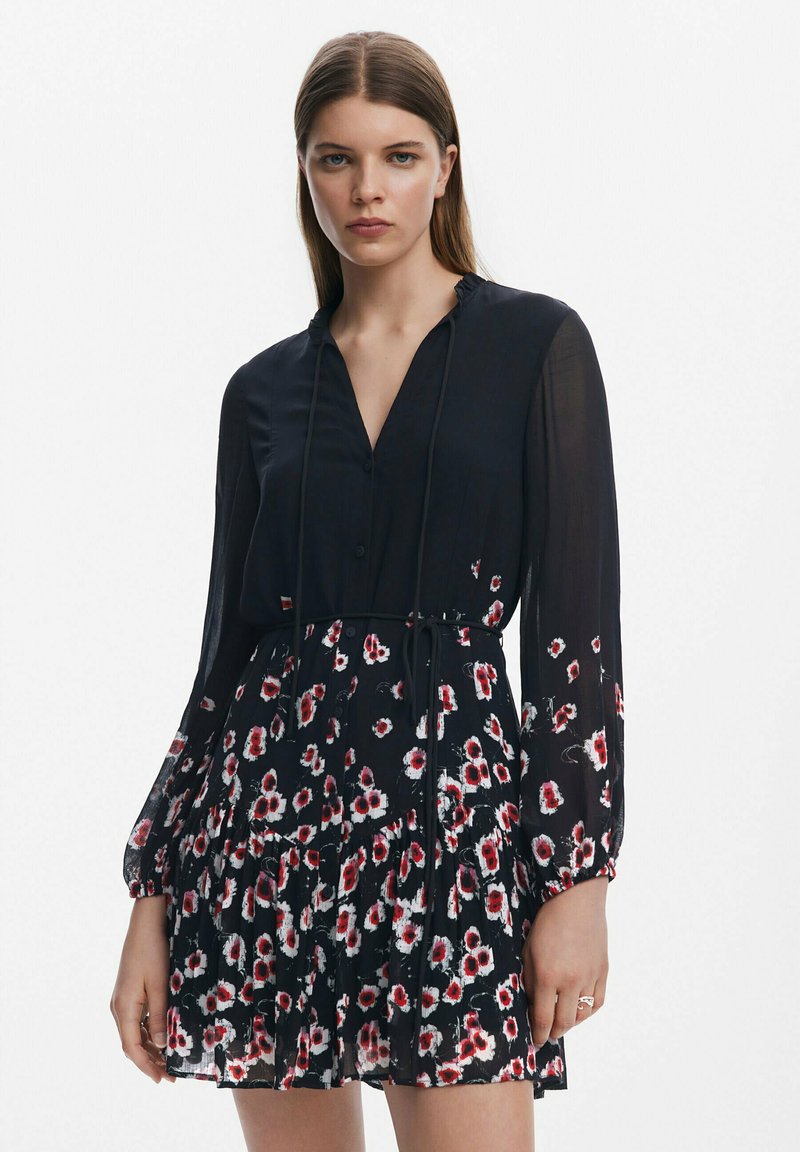 Schwarzes Kleid mit Knopfleiste, langen Ärmeln und Bindedetail. Hat ein florales Muster in Rot und Weiß sowie ein gestuftes Rockdesign.