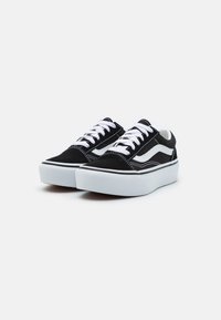 Zapatillas de gamuza negra con cordones blancos, que presentan una franja lateral blanca, una gruesa suela de goma blanca y detalles de costura en contraste.