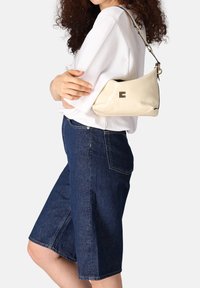 Crèmekleurige leren tas met een gebogen vorm, zwarte accenten, goudkleurige details en een diamantpatroon versiering aan de voorkant.