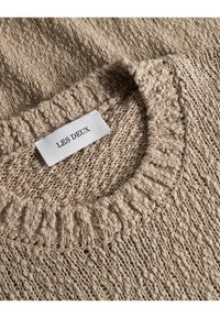 Jersey de punto beige con un patrón texturizado y cuello redondo acanalado. La etiqueta dice "LES DEUX". Construcción en hilo suave y grueso.