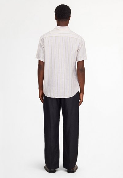 Man standing facing away wearing a short-sleeve, light striped shirt, black loose-fitting pants, and black shoes on white background.