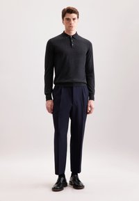 Dunkelgraues Langarm-Polohemd mit Kragen und drei Knöpfen, kombiniert mit navyblauen maßgeschneiderten Hosen und schwarzen Schnürschuhen.