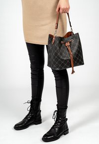 Borsa a secchiello nera con manici in pelle beige, caratterizzata da un motivo geometrico e chiusura a coulisse. Indossata con pantaloni in pelle nera e stivali con lacci.