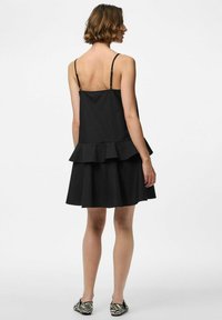 Mustakalaseta ilma varrukatega kleit kihiliste äärtega. Valmistatud siledast kangast, millel on istuv rinnahoidja. Tagantvaates on nähtavad reguleeritavad rihmad ja lõtv istuvus.