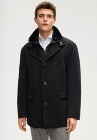 Cappotto nero in misto lana con colletto in pelliccia sintetica, doppie tasche frontali e chiusura con zip. Presenta una vestibilità aderente e dettagli con bottoni.