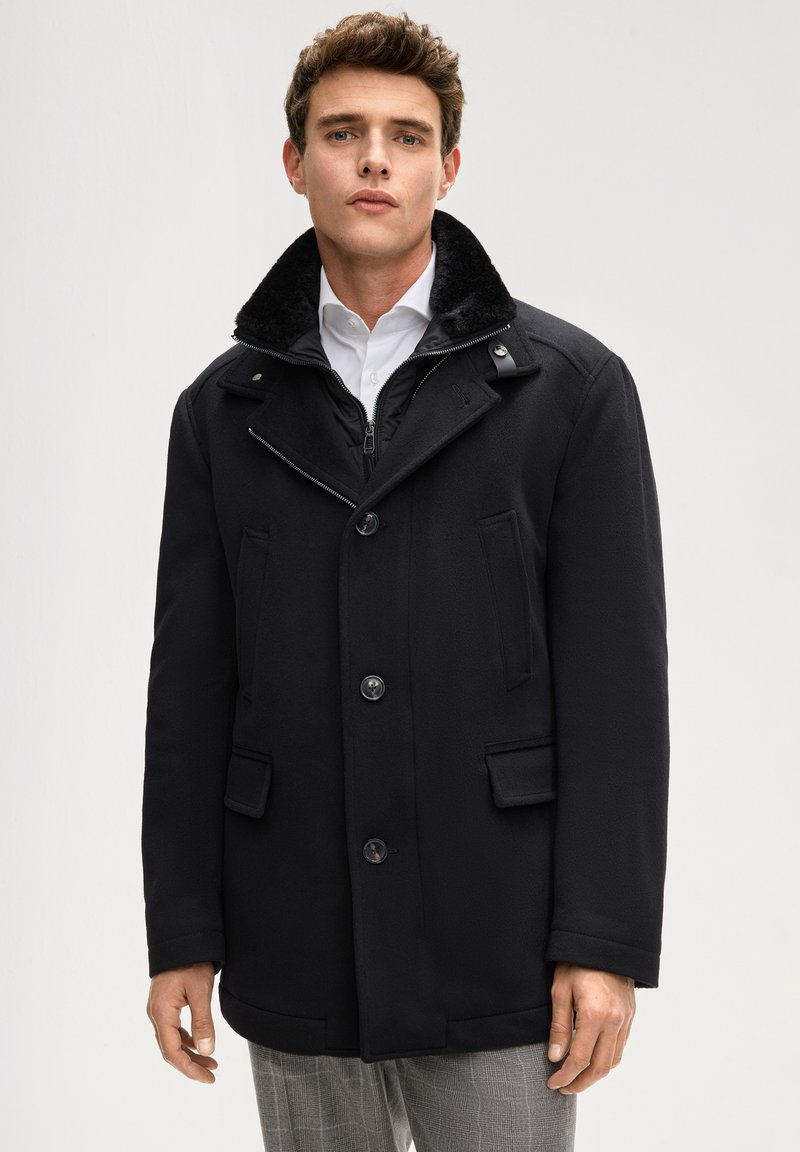 Cappotto nero in misto lana con colletto in pelliccia sintetica, doppie tasche frontali e chiusura con zip. Presenta una vestibilità aderente e dettagli con bottoni.