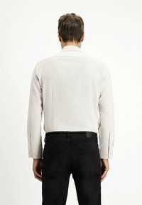 Camicia a maniche lunghe di colore chiaro con una texture liscia e polsini con bottoni, abbinata a jeans di denim neri con tasche posteriori.
