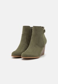Stivali alla caviglia verde oliva realizzati in suede, con tacco a zeppa, punta affusolata, zip laterale e dettaglio decorativo con fibbia sul tallone.
