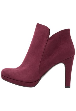 Bottine en cuir suédé bordeaux avec un talon haut, un orteil en amande et un design découpé à l'avant. Texture lisse avec une silhouette épurée.