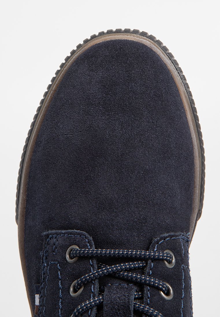 Zapato de ante azul marino con puntera redonda, parte superior texturizada, costuras en contraste y suela de goma oscura. Cuenta con cierre de cordones.