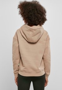 Sudadera beige con una gran capucha forrada, hombros caídos, puños de canalé y dobladillo inferior. Tejido de algodón suave con una textura lisa.