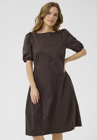 Rjava obleka do kolen s napihnjenimi rokavi, ki ima preprost okrogli izrez in gladko, lahko tkanino z lesketajočo se teksturo.