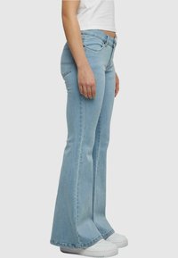Lichtblauwe flared jeans met een hoge taille, denim stof, zijzakken, stikseldetails en een lichte rafeling aan de uiteinden. In combinatie met witte sneakers.