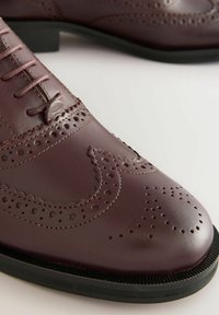 Chaussure brogue en cuir marron avec des perforations complexes et un design à bout ailé. Semelle en caoutchouc noir pour plus de durabilité, avec des accents cousus.
