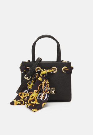 Bolso estructurado negro con asas superiores, detalles dorados, correa desmontable y un pañuelo estampado en negro y dorado atado a un lado.