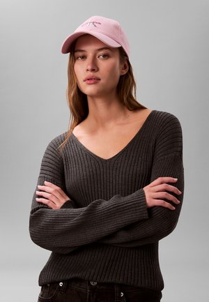 Szary prążkowany sweter z szerokim dekoltem w kształcie litery V i długimi rękawami, zestawiony z jasnoróżową czapką z daszkiem z haftowanym logo.