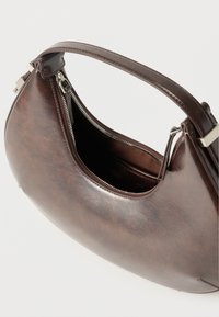 Σκούρο καφέ δερμάτινη τσάντα σε σχήμα ημισελήνου με μονή λαβή και κορυφαίο φερμουάρ, μερικώς ανοιχτό που αποκαλύπτει υφασμάτινη επένδυση.