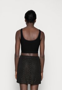 Black cropped top with textured fabric and wide straps paired with a black skirt featuring gold dot patterns. View from the back.