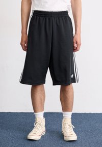 Sorte atletiske shorts lavet af blødt stof, med hvide vertikale striber langs siderne og en elastisk talje for komfort.