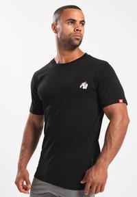 Zwarte T-shirt met korte mouwen van katoen. Heeft een kleine witte gorillaprint op de borst en een rode logo-tag op de mouw.