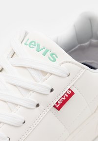 Valkoiset Levi's sneakerit valkoisilla nauhoilla, minttuvihreä Levi's-logo kielessä ja pieni punainen Levi's-kankainen etiketti sivussa.