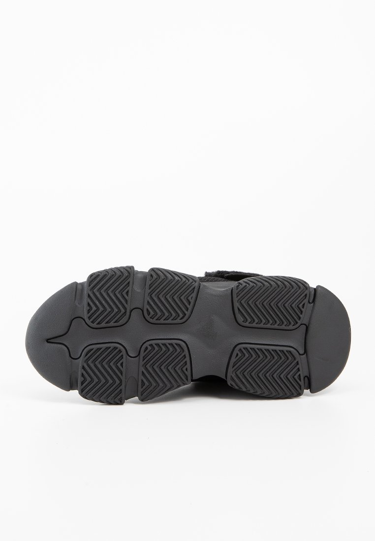 Podeszwa czarnego buta z widoczną bieżnią, przedstawiająca liczne wzory zygzakowate oraz segmentowane obszary uchwytu dla lepszej przyczepności, na białym tle.