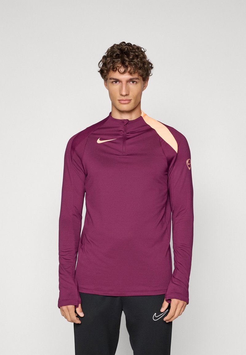 Langärmliges Sportshirt in Dunkellila mit einem Viertel-Reißverschluss, das einen helloranfarbenen Schulterakzent und ein kleines Nike-Logo auf der Brust aufweist.