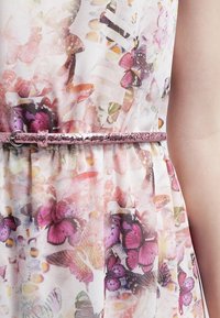 Blommig klänning med en fjärilsprint i rosa, lila och gula nyanser, åtsnörd i midjan med ett glittrande rosa bälte.