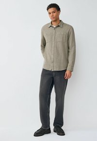 Gray flannel shirt with a button-down collar, two front pockets, and silver buttons, paired with dark jeans and black shoes.