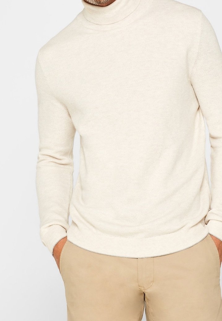 Pull beige à col roulé en tissu tricoté texturé. Coupe ajustée avec manches longues et ourlet côtelé, associé à un pantalon beige clair.