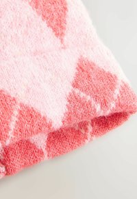 Weiche, gestrickte Decke in verschiedenen Rosa- und Koralltönen mit einem Diamantmuster. Die Textur ist plüschig und warm, mit einem gefalteten Randdetail.